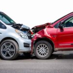 Head-on car collision between a silver vehicle and a red SUV, showing severe front-end damage after a traffic accident.