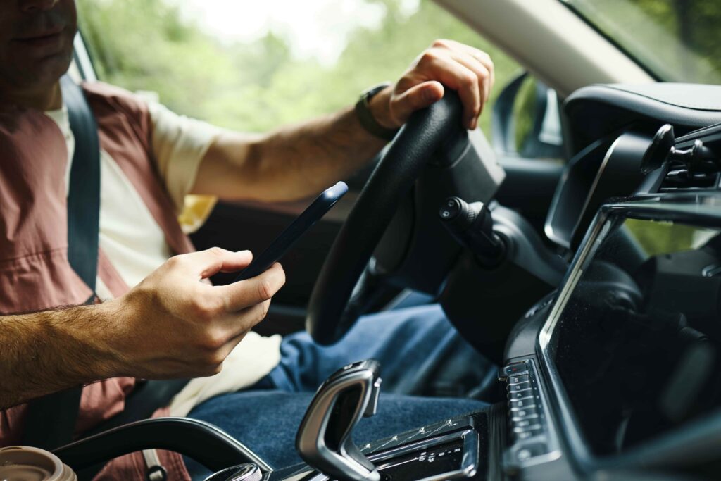 Driver using a smartphone while driving a car, illustrating distracted driving and mobile phone use behind the wheel.