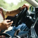 Driver using a smartphone while driving a car, illustrating distracted driving and mobile phone use behind the wheel.